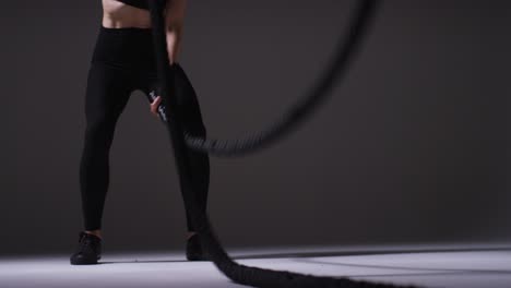 Close-Up-Studio-Shot-Of-Mature-Woman-Wearing-Gym-Fitness-Clothing-Doing-Cardio-Exercise-With-Battle-Ropes